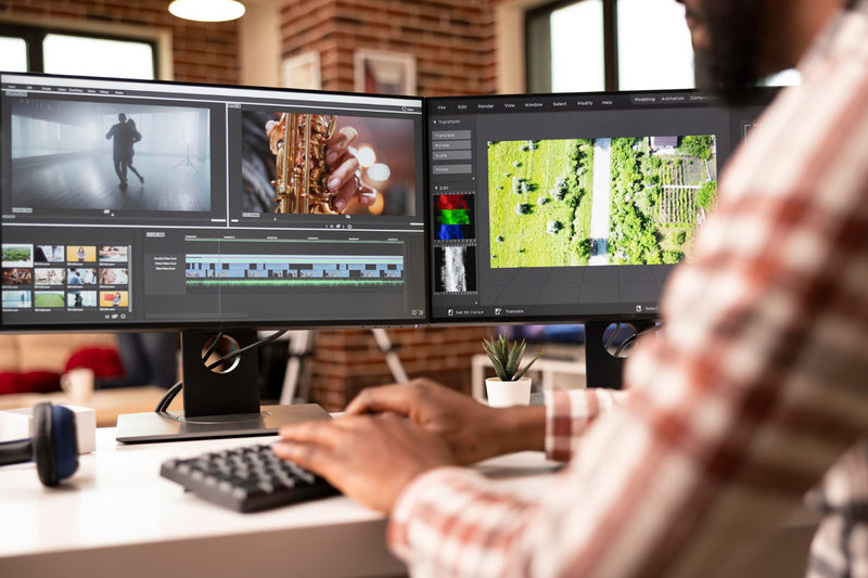 Person working on video editing software on a dual-monitor setup in a home office.
