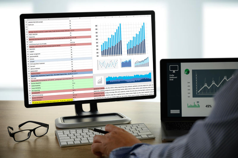 Person working at a desk with a computer displaying financial charts and a tablet showing graphs.