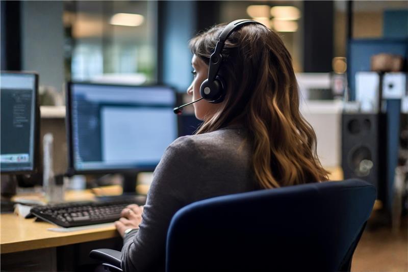 Person wearing a headset in an office setting with multiple monitors.
