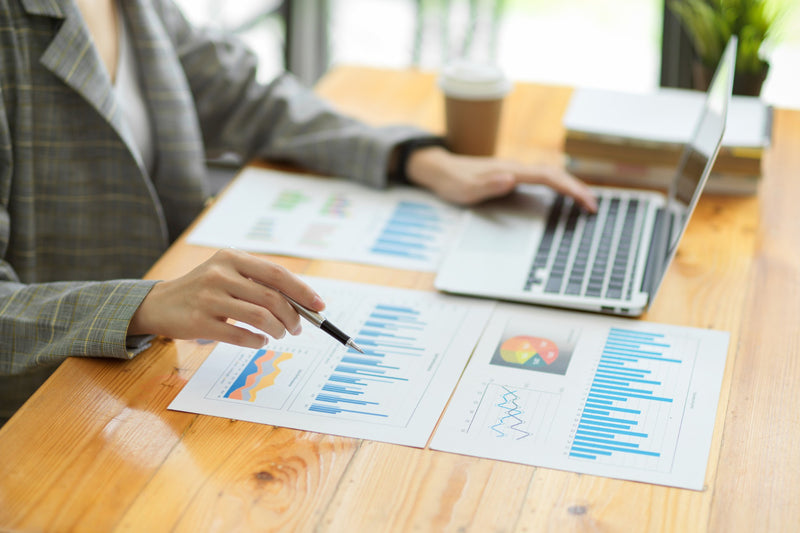 Person analyzing financial reports with a laptop on a wooden desk