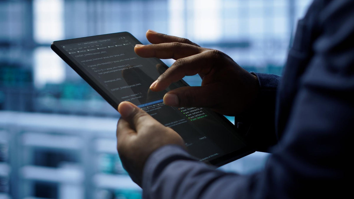 Person using a tablet with code on the screen in a blurred indoor setting by menko services