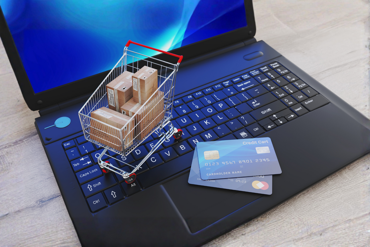 Laptop with a shopping cart filled with boxes and two credit cards on a wooden surface  by menko services